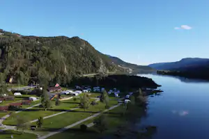 Campingplatz am See im Tal mit Rasenparzellen, Wegen und Wohnwagen, umgeben von bewaldeten Hügeln.