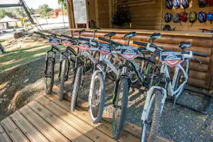 Mehrere Fahrräder stehen unter einem Holzunterstand am Campingplatz, mit Schildern und Reifen auf dem Boden.