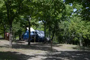 Stellplatz auf dem Campingplatz mit Zelt, Auto und Vorzelt zwischen Bäumen, auf Kiesboden.