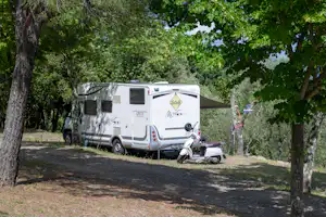 Wohnmobil auf einem Stellplatz im Grünen, neben einem Motorrad und unter Bäumen am Weg.