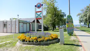 Weg auf dem Campingplatz mit Blumenbeet, Schildern für SUP und Yoga sowie Gebäuden und Bäumen im Hintergrund.
