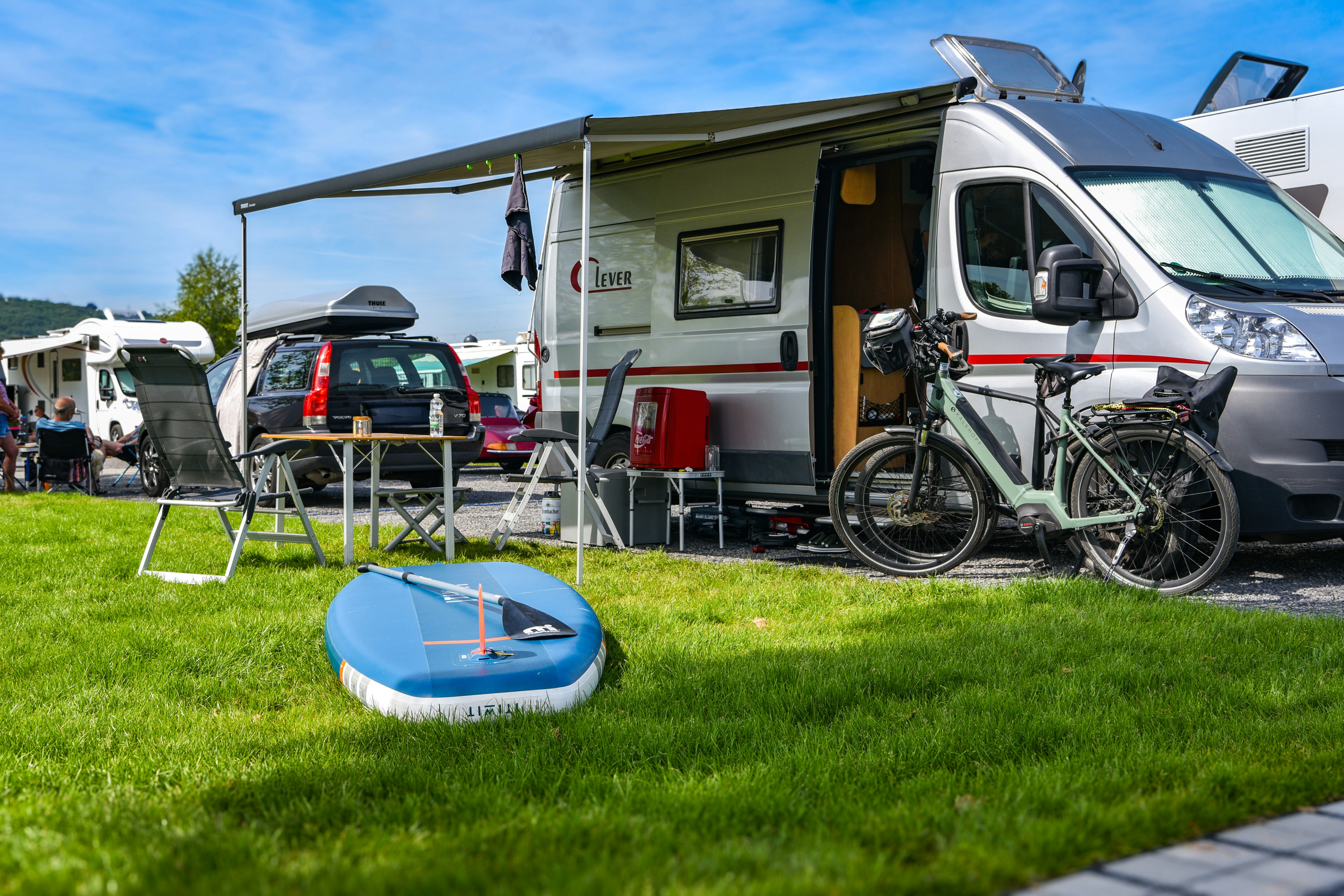 Wohnmobil mit Fahrrad und Markise am Campingplatz, daneben Tisch und Stühle, im Vordergrund Planschbecken auf Rasen.