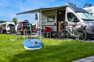 Wohnmobil mit Fahrrad und Markise am Campingplatz, daneben Tisch und Stühle, im Vordergrund Planschbecken auf Rasen.