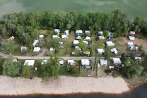 Campingplatz am Fluss mit vielen Stellplätzen, Wohnwagen und Zelten, umgeben von Bäumen und Wegen.