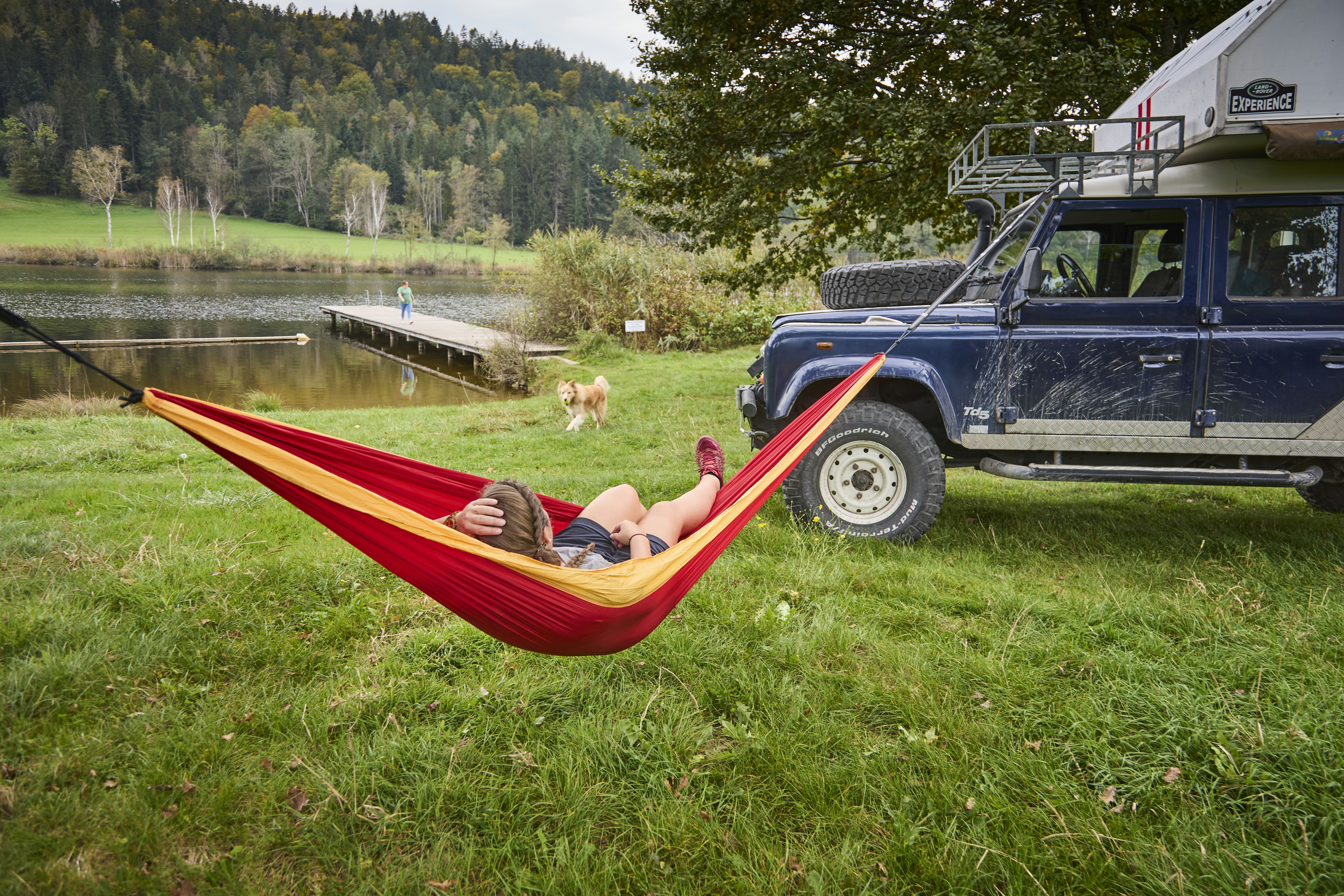Family-Camping Hafnersee - Camperin mit Hund liegt in einer Hängematte am Ufer des Sees