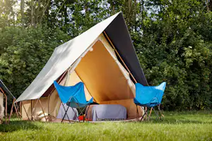 Großes Campingzelt mit Vorraum und zwei blauen Campingstühlen auf einer Wiese am Waldrand.