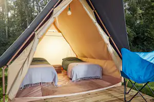 Offenes Zelt auf einem Holzdeck mit zwei Betten und Stuhl, im Hintergrund Bäume im Campingbereich.
