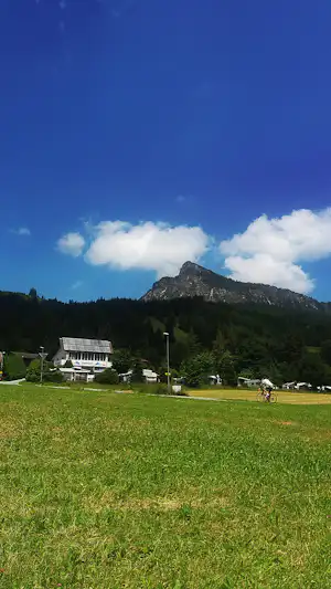 Campingwiese mit Blick auf Berge, ein Gebäude mit Terrasse und ein Fahrrad auf dem Weg.
