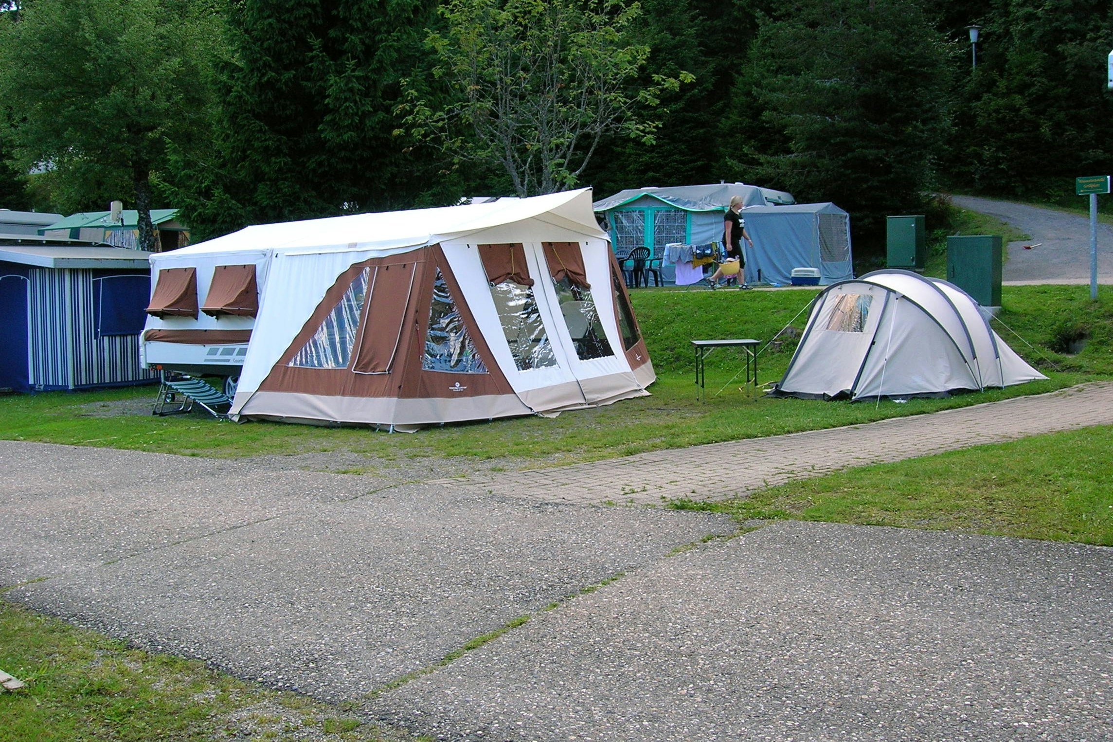Großes Zelt und weiteres Campingzelt auf einer Wiese am Campingplatz, mit Bäumen im Hintergrund.