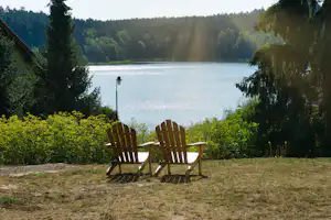 Zwei Holz-Gartensessel auf einer Wiese mit Blick auf den See, umgeben von Bäumen und Waldhängen.