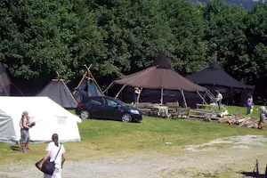 Campingplatz mit mehreren Zelten, geparktem Auto und Picknicktisch im Grünen am Waldrand.