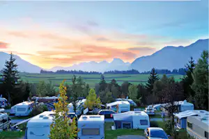 Campingplatz mit Wohnwagen und Stellplätzen, Blick ins Tal mit Wiesen, Bäumen und Bergen in der Ferne.
