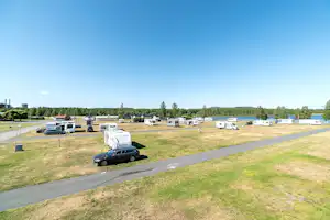 Campingplatz mit Wohnwagen und Stellplätzen, gepflasterter Zufahrtsstraße und Blick auf einen See in der Ferne.