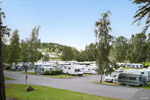 Wohnmobile und Caravans auf einem Campingplatz, umgeben von Rasen, Bäumen und einer breiten Zufahrtsstraße.