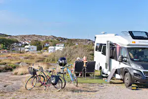 Wohnmobil auf dem Stellplatz mit Fahrrädern, Campingstühlen und weiteren Fahrzeugen im Hintergrund vor einer felsigen Landschaft.