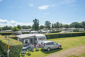 Wohnmobil auf dem Stellplatz mit Auto davor, Sitzgruppe unter Markise und Hecken im Campinggelände.