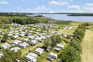 Luftaufnahme eines Campingplatzes mit Wohnmobilen und Stellplätzen, grünen Wegen und einem nahegelegenen See mit Uferlinie.
