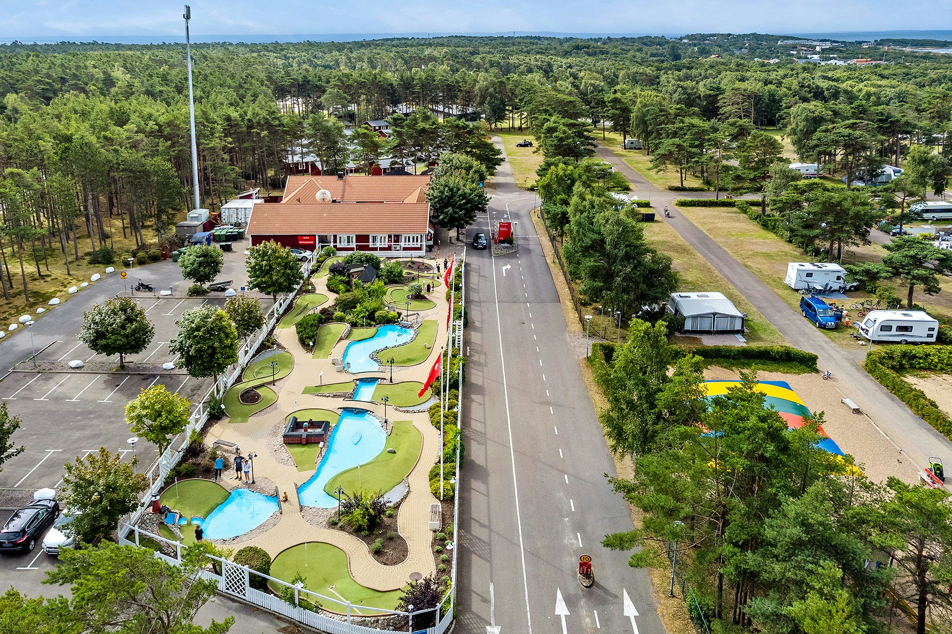 Luftaufnahme eines Campingplatzes mit Schwimmbecken, gepflegten Wegen, Stellplätzen und Wohnmobilen, umgeben von Bäumen und Häusern.