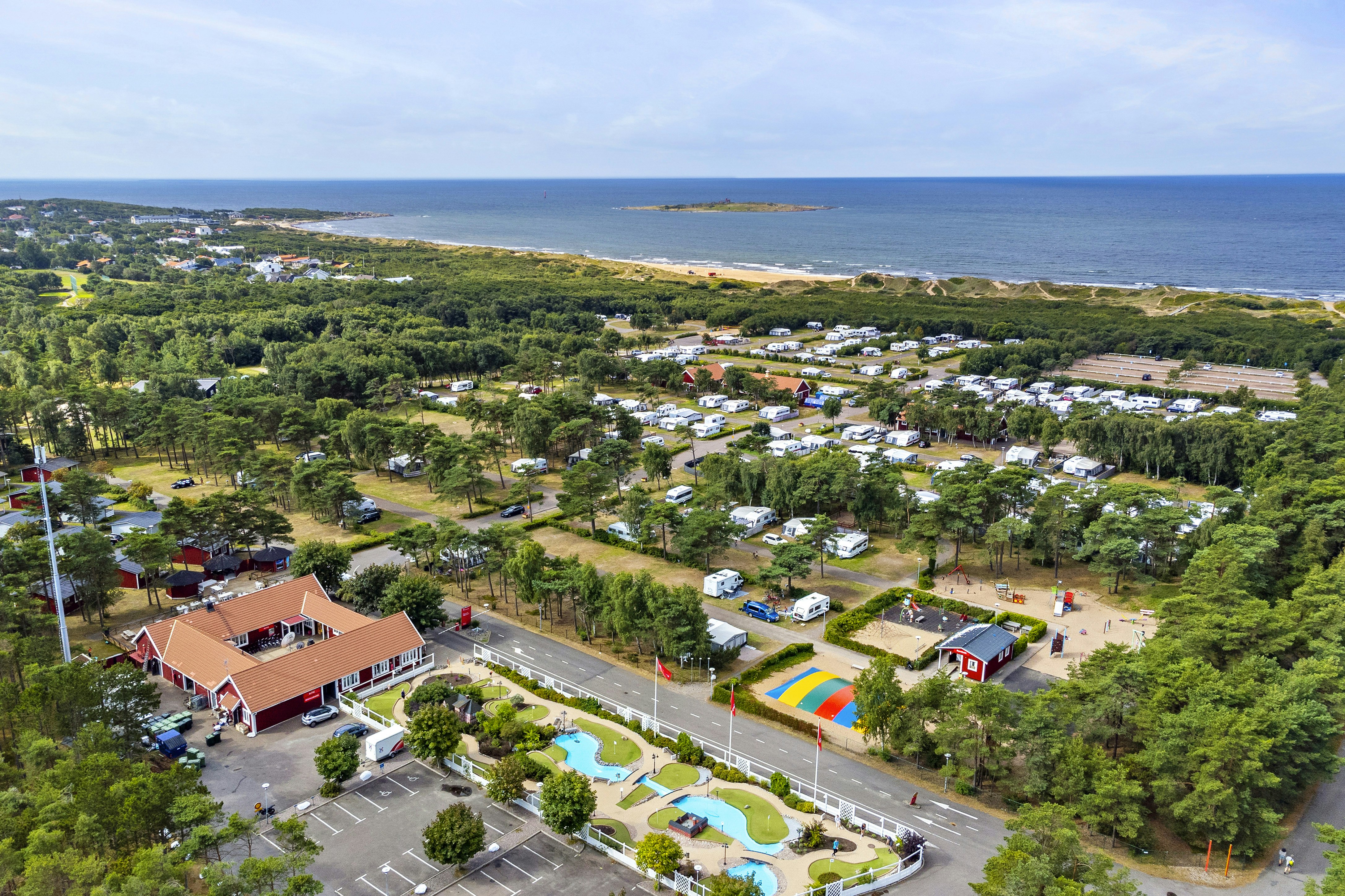 Luftaufnahme eines Campingplatzes mit Stellplätzen, Wohnwagen und Zelten, Wegen, Pool und Blick auf das Meer.