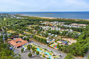 Luftaufnahme eines Campingplatzes mit Stellplätzen, Wohnwagen und Zelten, Wegen, Pool und Blick auf das Meer.