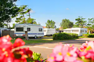 Wohnwagen und Wohnmobil auf einem Campingplatz, Blick auf Stellplätze mit Rasen, Hecken und Bäumen bei Tageslicht.