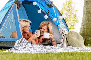 Blaues Campingzelt mit Lichterkette, zwei Personen sitzen davor und halten Kaffeetassen in der Hand.