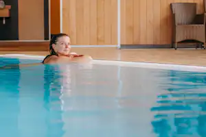 Frau im Poolbecken, Kopf und Schultern über dem Wasser, im Hintergrund Holzverkleidung und Liegen am Beckenrand.