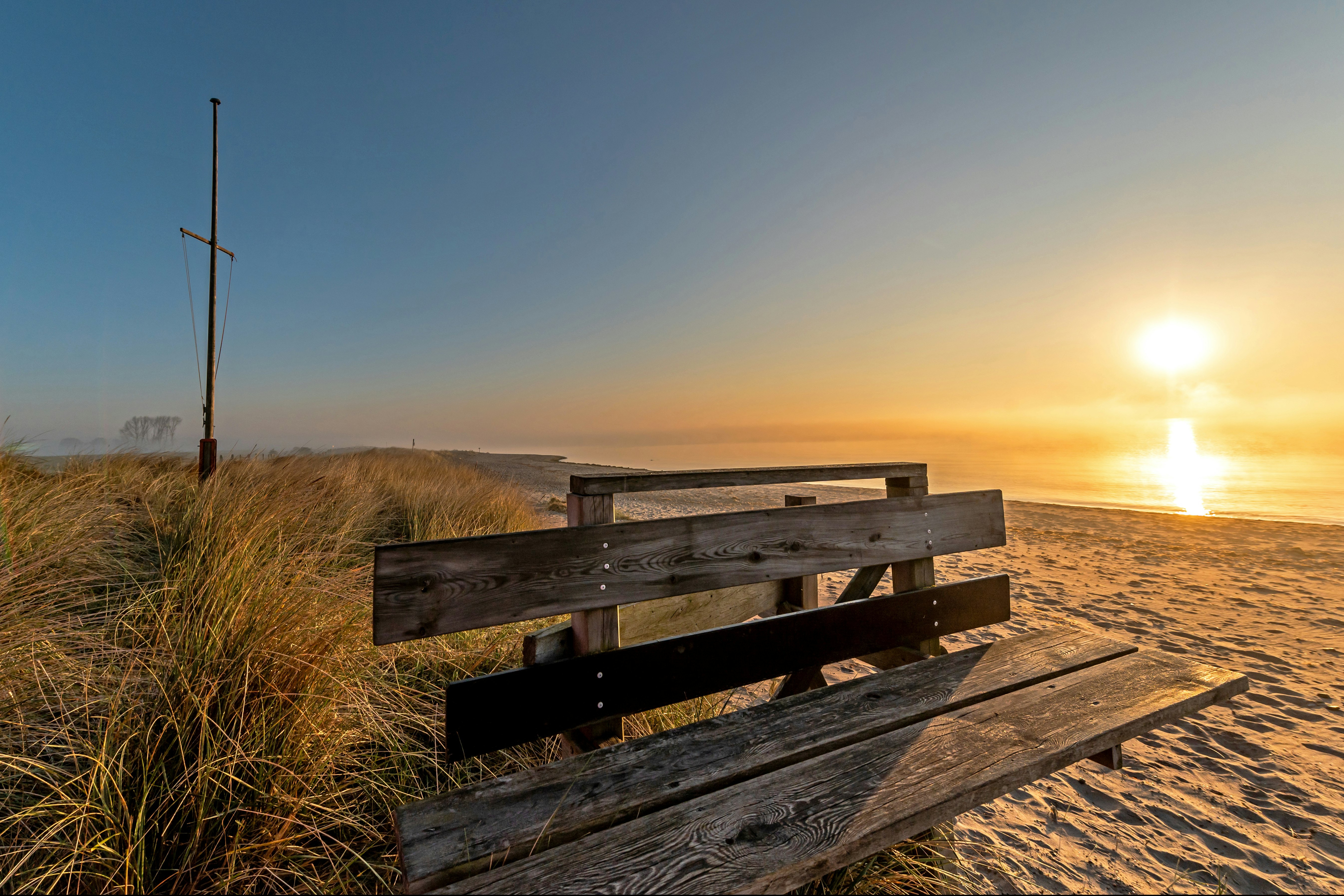 FKK Camping Ostsee Rosenfelder Strand - Blick auf eine Bank am Strand bei Sonnenuntergang