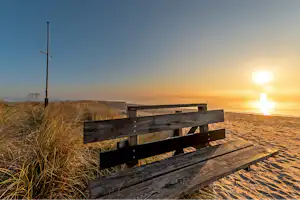 FKK Camping Ostsee Rosenfelder Strand - Blick auf eine Bank am Strand bei Sonnenuntergang