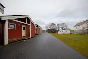 Reihen von roten Ferienhäusern mit Eingangstüren und überdachten Veranden, asphaltierter Weg und Rasenfläche neben dem Campingplatz.