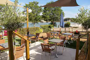 Terrasse am Campingplatz mit Sitzgarnitur, Sonnenschirm und Blick auf den See, Bäume und Garten am Ufer.