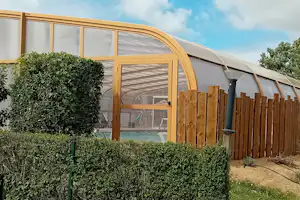 Wohnwagen mit Veranda und Holzsichtschutzzaun, davor Hecken und ein Weg auf dem Campingplatz.