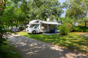 Wohnmobil auf einem Stellplatz im Grünen, mit Vorzelt und Tisch, umgeben von Bäumen und einem gepflasterten Weg.