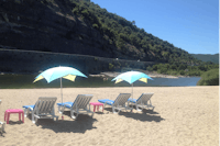 Flower Camping Le Riviera - Sandstrand vom Campingplatz am Fluss mit Liegestühlen, Sonnenschirmen und Blick auf Berge
