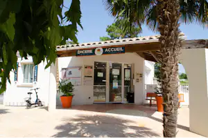Rezeption und Epicerie am Campingplatz mit Schildern, Eingangstür, Infotafeln und Fahrrädern neben dem Gebäude.