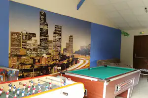 Kicker-Tisch mit grüner Spielfläche vor einer Wand mit Stadtbild und beleuchteter Straße, im Innenraum.