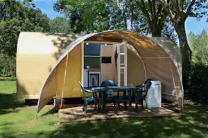 Coco Sweet Zelt mit offener Tür, Holzterrasse und Tisch mit Stühlen im Grünen, umgeben von Bäumen.