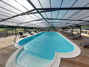 Beheizter Campingpool unter einem Glasdach mit Liegen auf Holzdeck und Blick auf die Seitenwände der Überdachung.