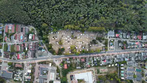 Luftaufnahme eines Campingplatzes mit Stellplätzen, Wegen, Gebäuden und vielen Bäumen im Hintergrund.