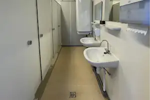Flur im Camping-Badebereich mit zwei Waschbecken, Spendern und Türen, daneben ein großer Boiler an der Wand.