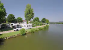 Wohnmobile und Campingplätze am Ufer eines Sees, mit Bäumen, Grasstreifen und einem kleinen Steg am Rand.