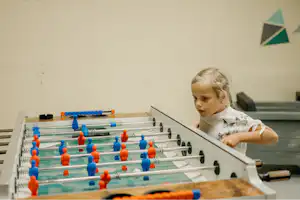 Ein Kind spielt an einem Tischkicker mit bunten Figuren in einem hellen Spielbereich.
