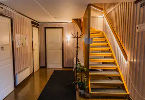 Flur in einem Campinghaus mit Holztreppe, weißen Türen, Wandlampen und Pflanzenkübel am Boden.