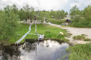 Holzsteg und Sitzbereich am kleinen Wasserbecken im Campingbereich, umgeben von Rasen, Bäumen und Wegen.