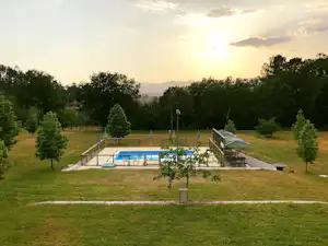 Schwimmbecken auf einem Campingplatz mit Liegen und Zaun, umgeben von Rasen und Bäumen bei Abendlicht.