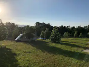 Zelt auf einer Campingwiese mit Bäumen und Büschen, im Hintergrund ein Wohnwagen und eine weite Landschaft.