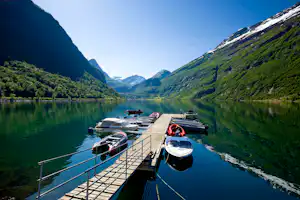Steg am See mit mehreren Motorbooten, umgeben von grünen Bergen und spiegelndem Wasser im Tal.
