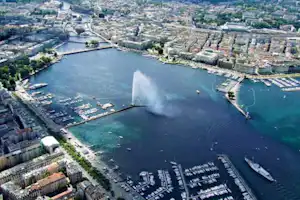 Blick auf einen Hafen mit Booten, Stegen und einem Wasserwehr im Fluss, umgeben von Gebäuden und Straßen.