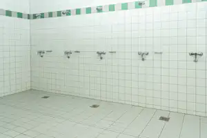 Duschraum mit gefliesterter Wand, mehreren Wandarmaturen und Bodenabläufen im Eckbereich.