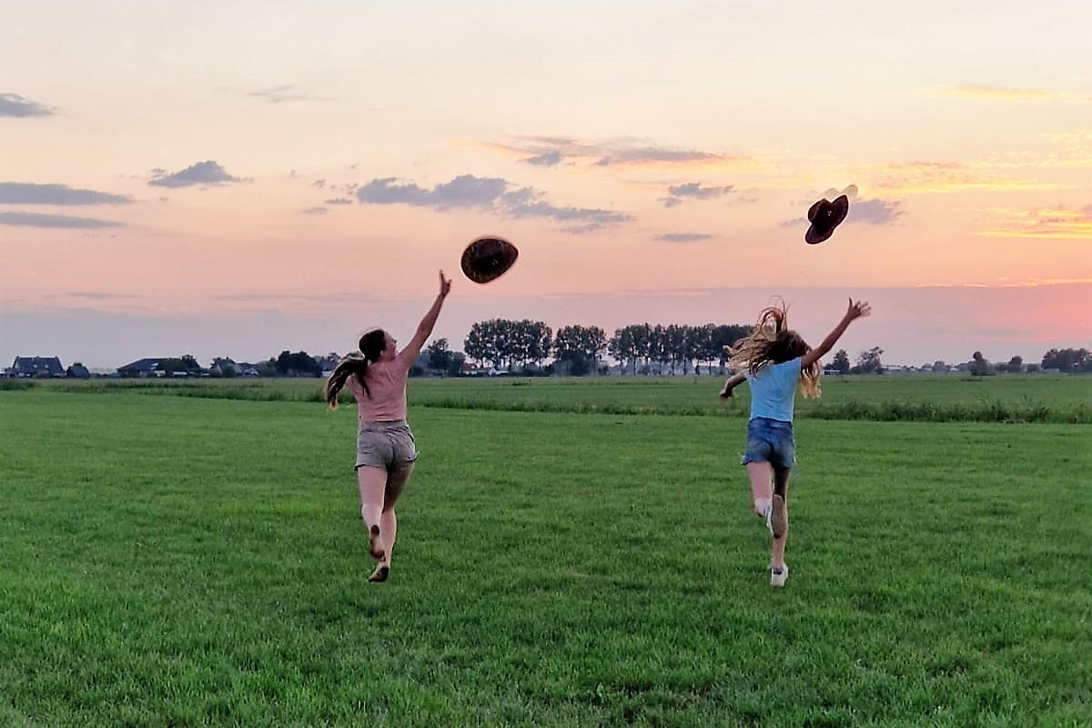 Glamping Camping Nix Hoeve - Mädchen auf Wiese werfen Hüte in die Luft